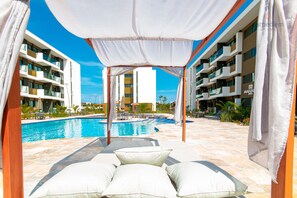 A poolside area with a canopy, lounge chairs, and a view of a modern building with balconies.