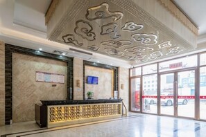 A hotel reception area with a marble reception desk, a bulletin board, and a large window with a view of the street. - Yihao Hotel (Xianyou)