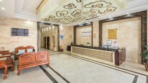 Een hotel lobby met een receptiebalie, een grote spiegel, een televisie en een zitgedeelte met een decoratief plafond.