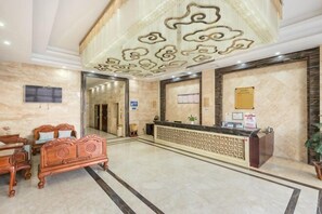 A hotel lobby with a reception desk, a large mirror, a television, and a reception area with a decorative ceiling.
