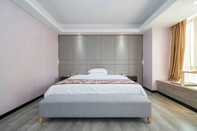 Una habitación de hotel moderna con una cama grande, un cabecero con iluminación integrada, una mesita de noche y un ventanal con cortinas.