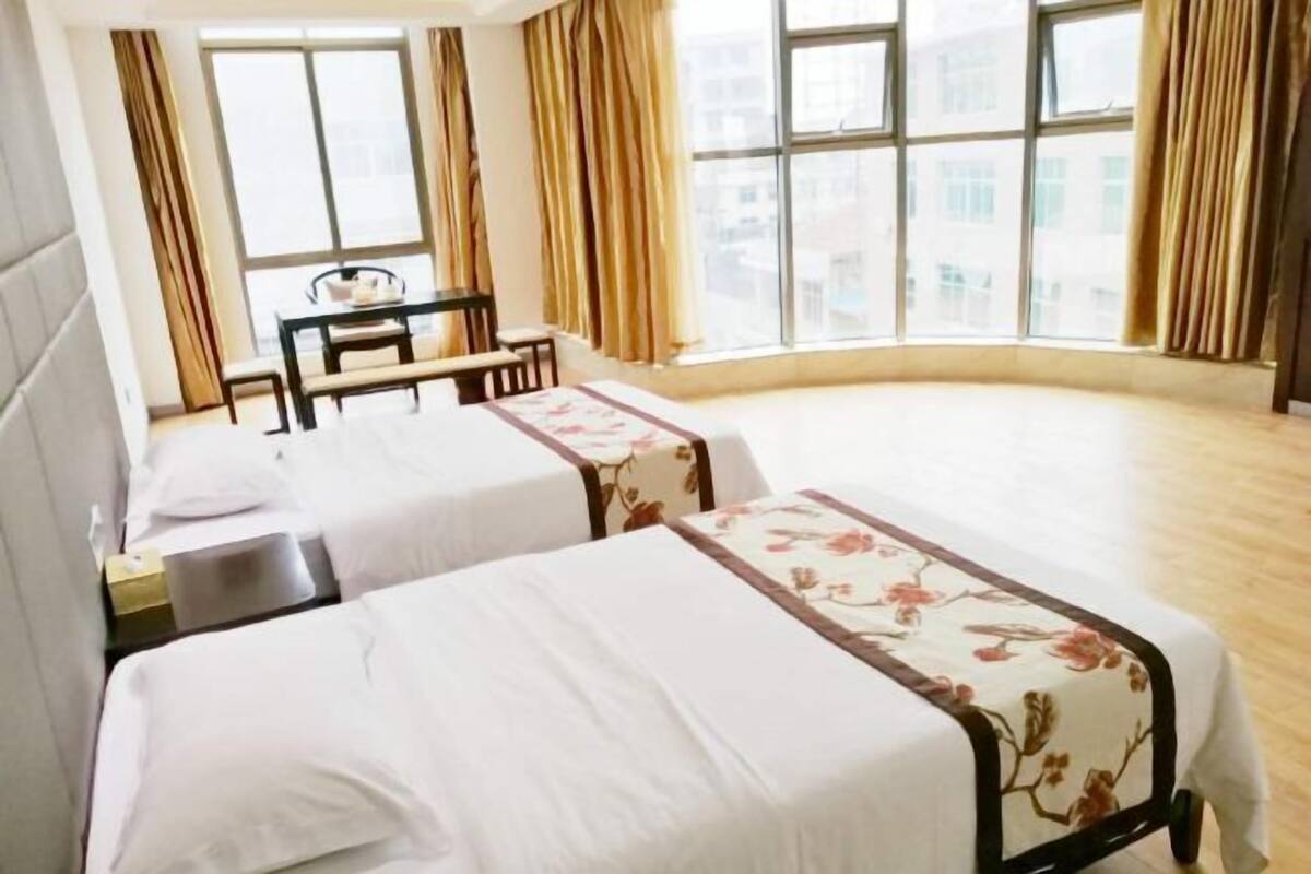 Quarto de hotel com duas camas, uma escrivaninha e vista da cidade através de amplas janelas.