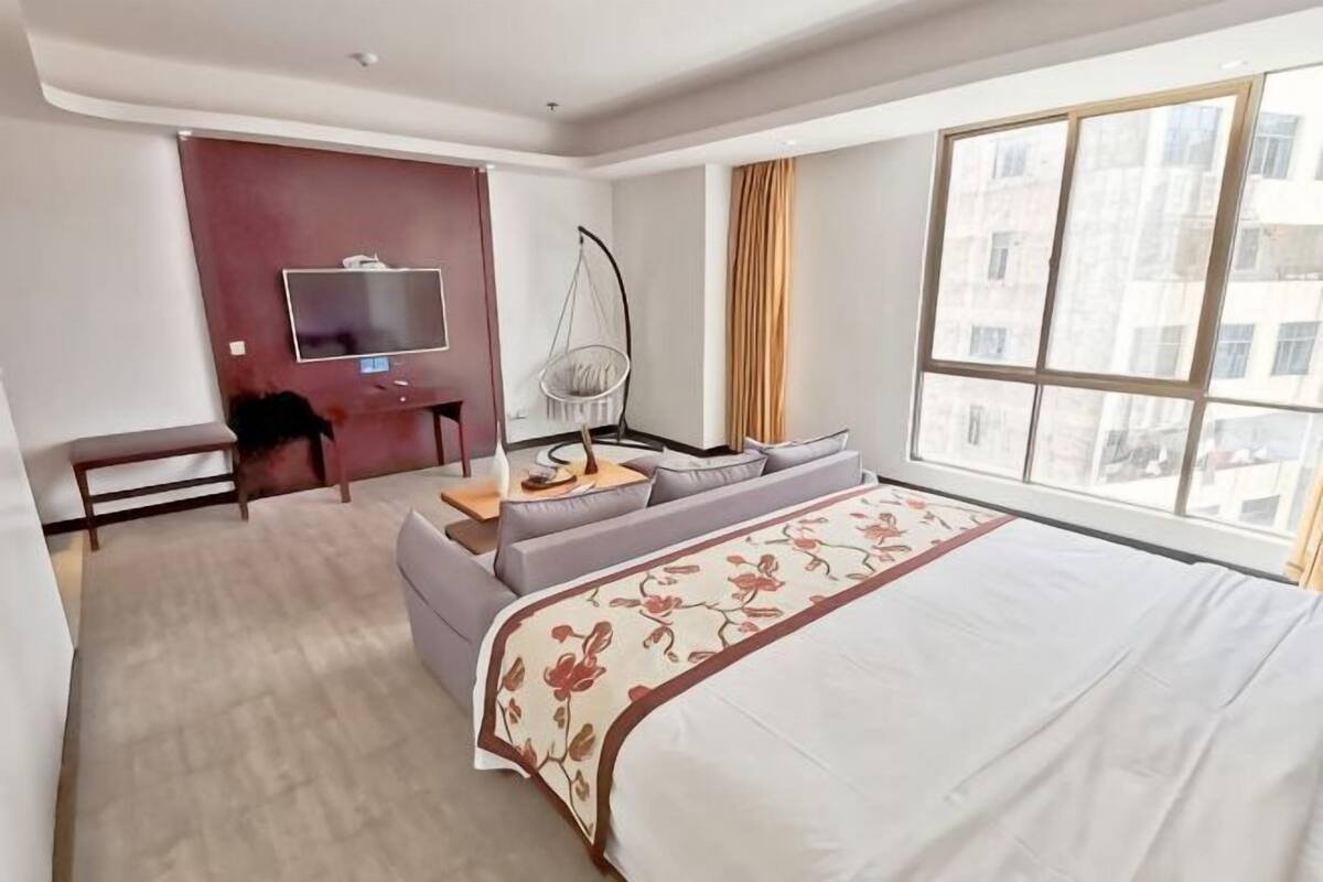 Quarto de hotel com uma cama grande, um sofá, uma escrivaninha com cadeira, uma televisão e uma janela com vista para edifícios.