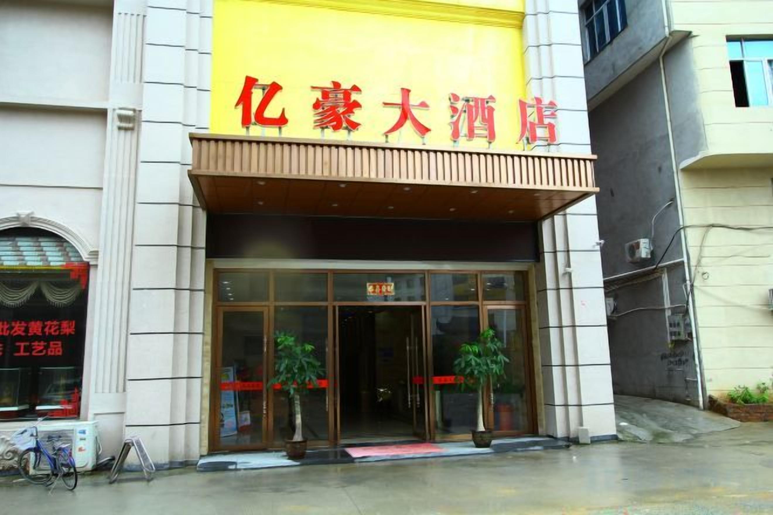 A building with a large yellow sign, a glass entrance, and potted plants outside.