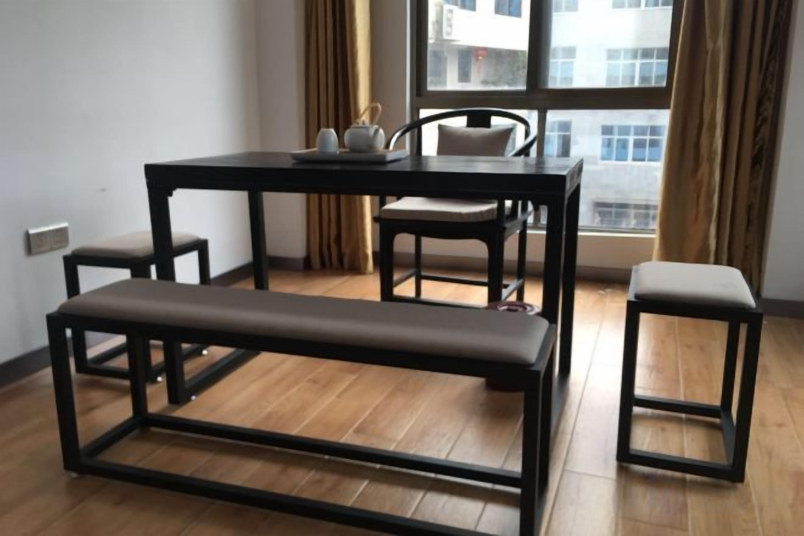 Een kamer met een houten vloer, een zwarte tafel met stoelen, een bank en een raam met gordijnen.