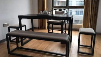 Een kamer met een houten vloer, een zwarte tafel met stoelen, een bank en een raam met gordijnen.
