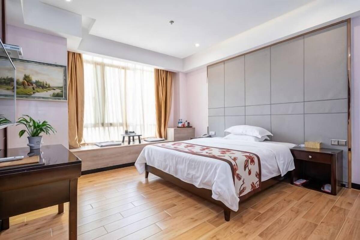 Quarto de hotel com cama grande, mesa de cabeceira, escrivaninha e uma cadeira.