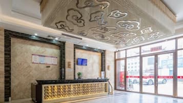 Een hotel receptie met een marmeren balie, een groot raam met uitzicht op de straat en een decoratief plafond.