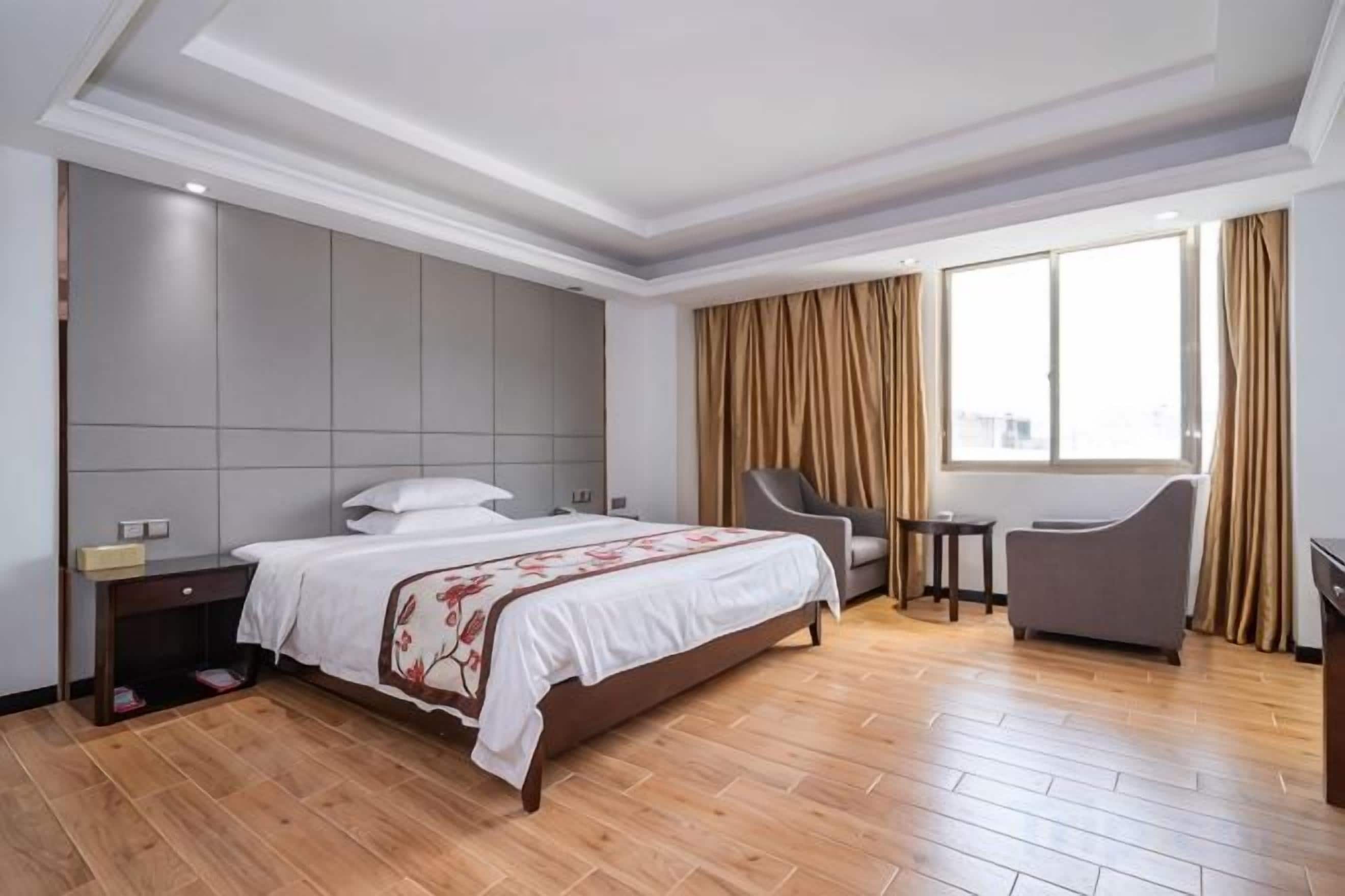 A hotel room with a large bed, a desk, a chair, and a window with curtains.