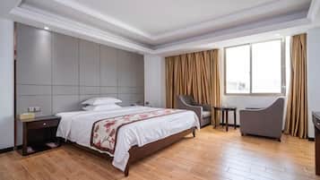 A hotel room with a large bed, a desk, a chair, and a window with curtains.