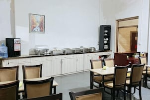 Un comedor con mesas y sillas, un refrigerador, una cafetera y un microondas.