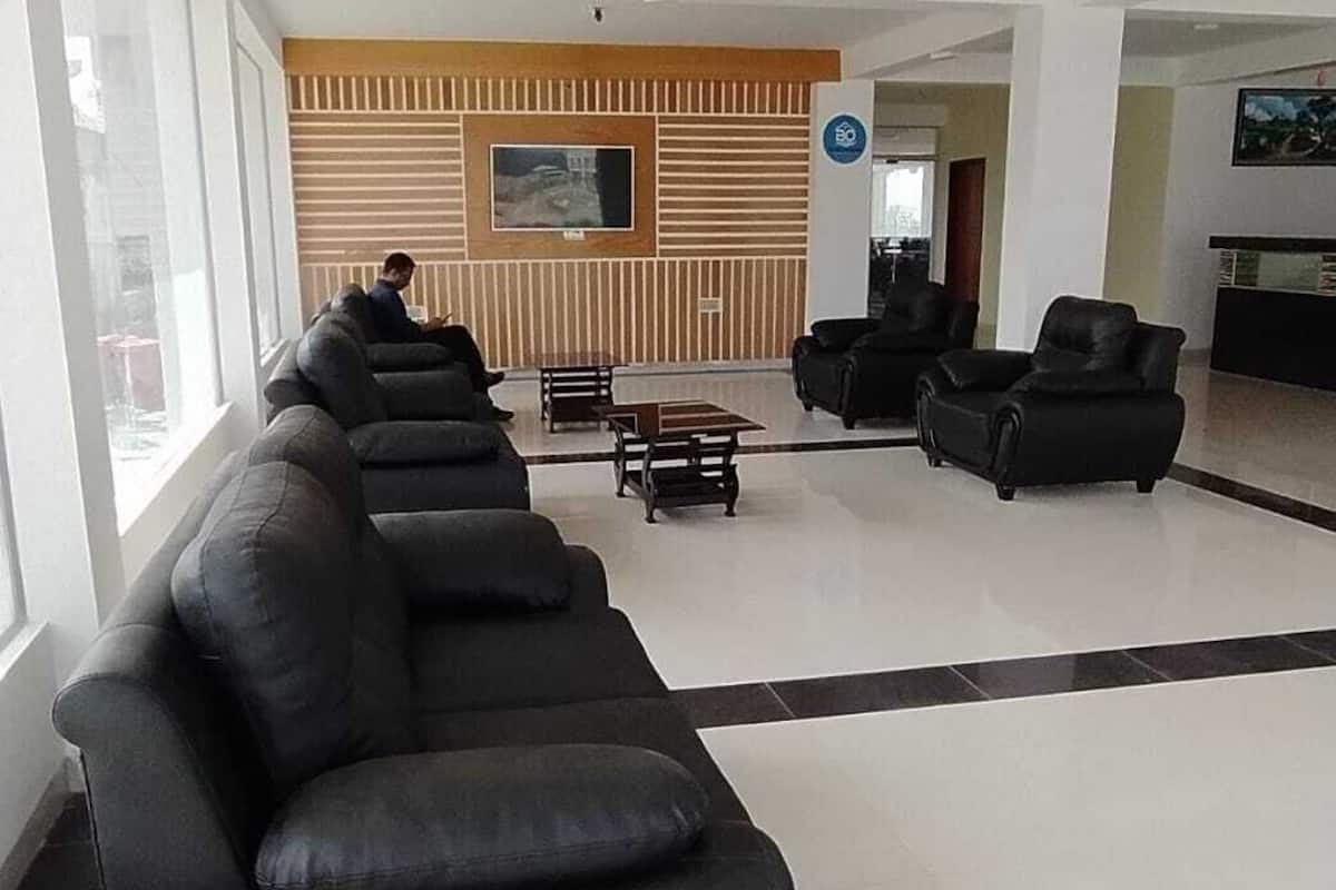 A spacious lobby with black leather sofas, a wooden reception desk, and a television screen.