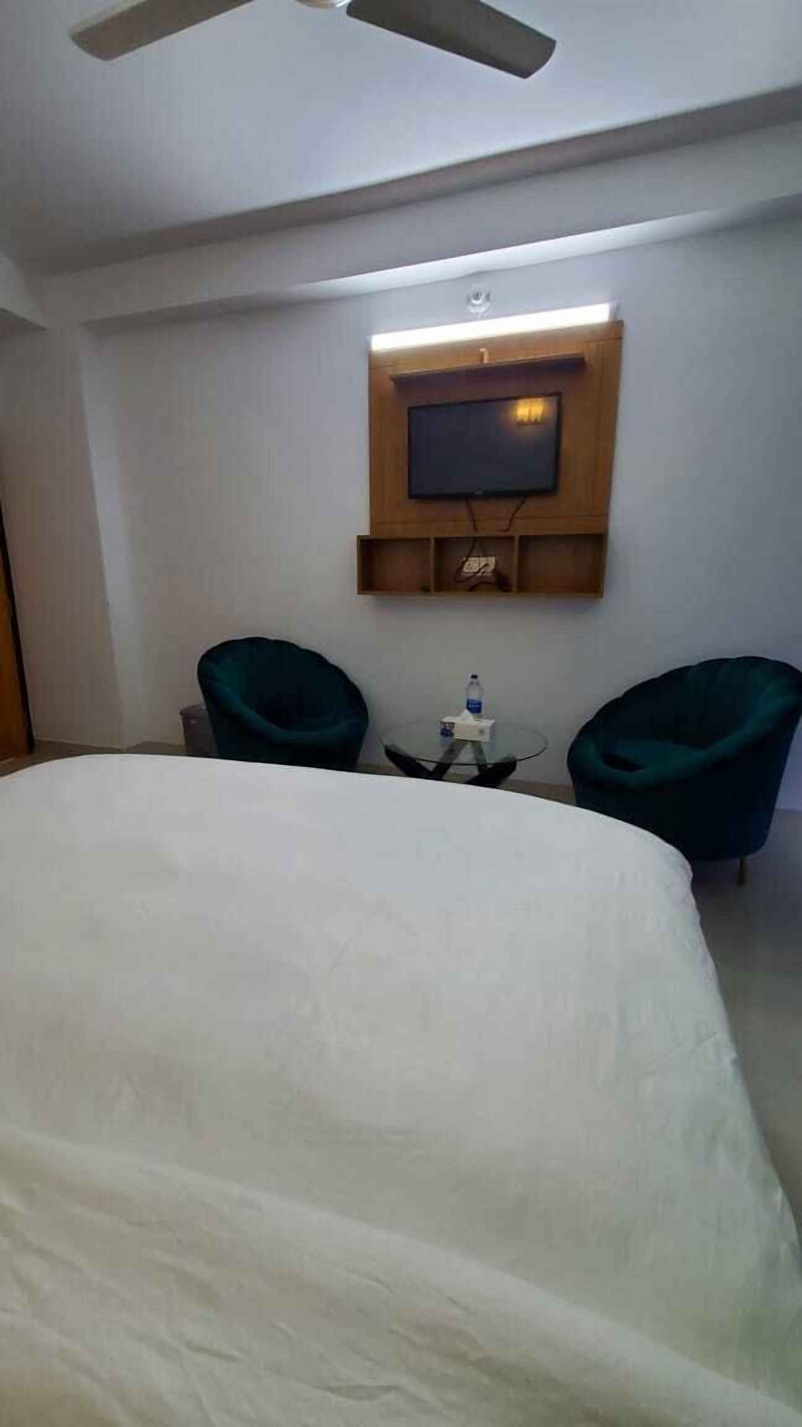 Une chambre d’hôtel avec un lit, deux chaises, une petite table et un téléviseur fixé au mur.