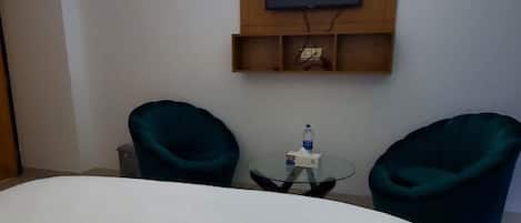 Une chambre d’hôtel avec un lit, deux chaises, une petite table et un téléviseur fixé au mur.