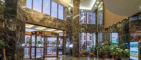 A lobby with marble flooring, large windows, and a chandelier.