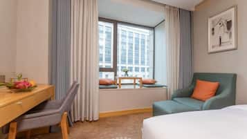 Una habitación de hotel con cama, escritorio con silla, ventana con cortinas y un sillón verde.