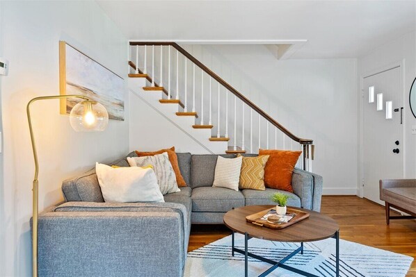 A modern living room with a grey sofa, a coffee table, and a staircase with wooden steps and white railings.