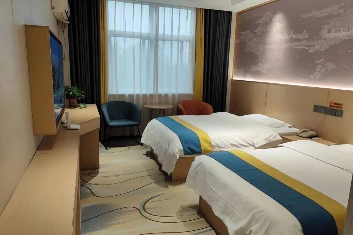 Una habitación de hotel con dos camas, un escritorio, una silla, una mesita y una ventana con cortinas.