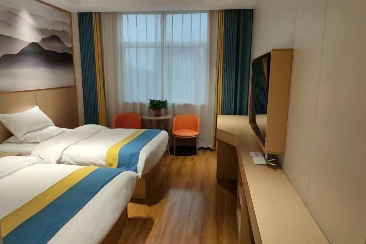 Habitación de hotel con dos camas, una mesita con una silla, televisor y ventana con cortinas.