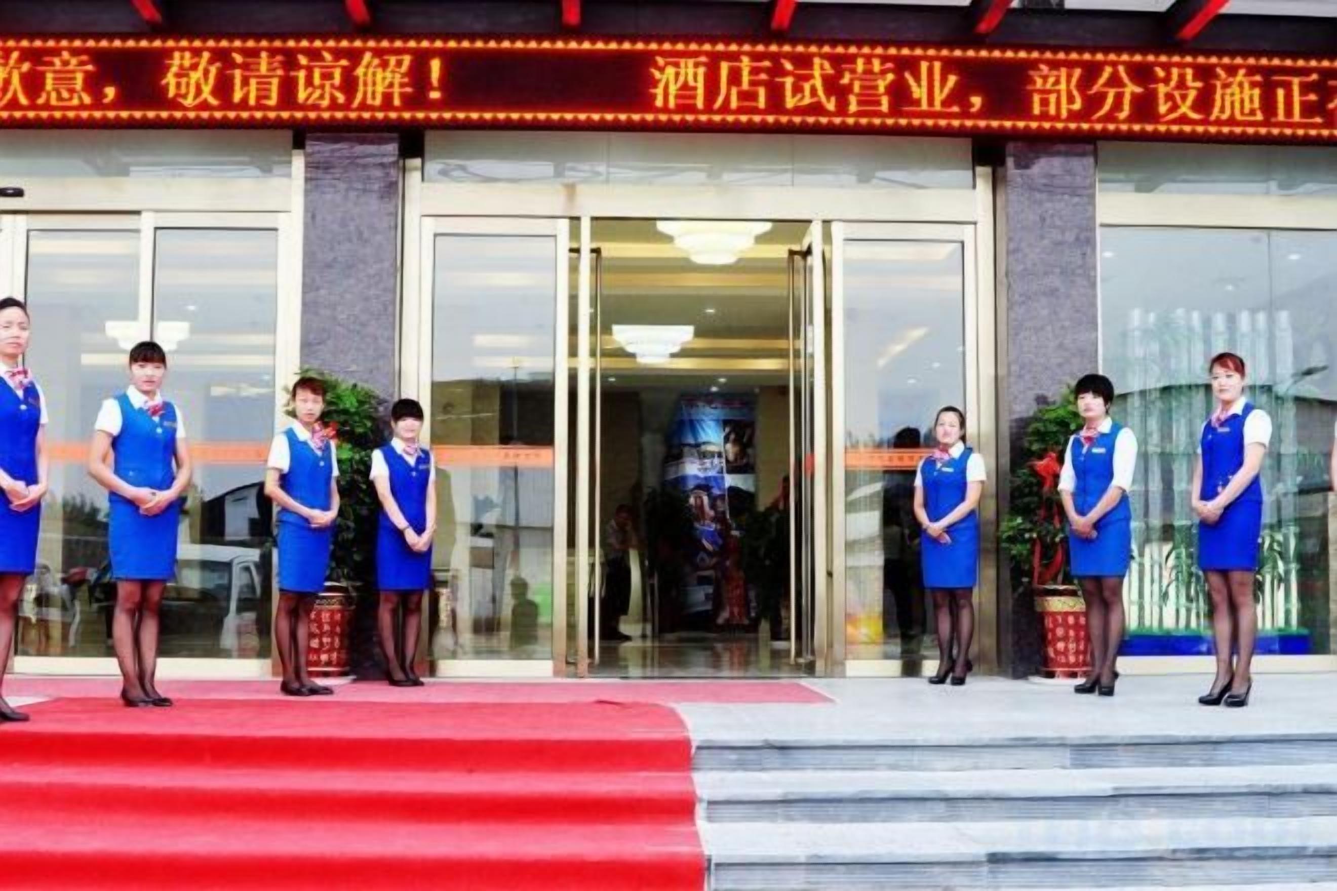 A group of uniformed individuals standing in front of a hotel entrance with a red carpet and a sign above.
