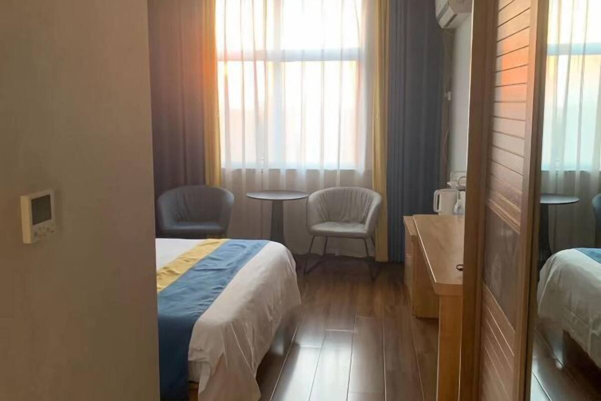 Una habitación de hotel con una cama, dos sillas, una mesita y un ventanal con cortinas.
