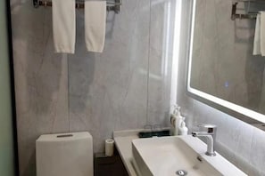 Ein modernes Badezimmer mit einem großen Spiegel, einem weißen Waschbecken und einem Handtuchhalter.