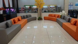 Een ruime lobby met een gebogen zithoek van grijze en oranje banken, een centrale gele boom en een uitzicht op het exterieur door grote ramen.