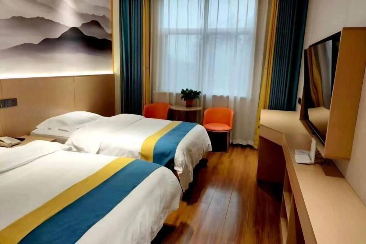 Habitación de hotel con dos camas, una mesa pequeña con sillas, un televisor y una ventana con cortinas.