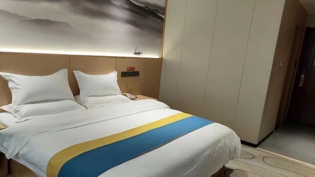 Een hotelkamer met een bed, een hoofdeinde, een muur met een schilderij en een deur.