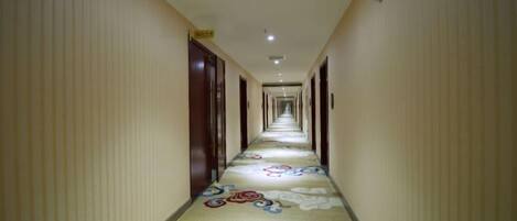 Un largo pasillo de hotel estrecho, con alfombra estampada y puertas a ambos lados.