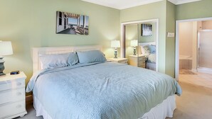 Quarto com uma cama grande, duas mesas de cabeceira com luminárias, um espelho e vista para o banheiro.