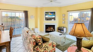 Sala de estar com sofá, mesa de centro, televisão, lareira e varanda com vista para a cidade.
