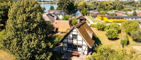 A traditional house with a thatched roof, surrounded by lush greenery and a lake in the background.
