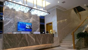 Una mesa de recepción con pantalla digital, paredes de mármol y una escalera.