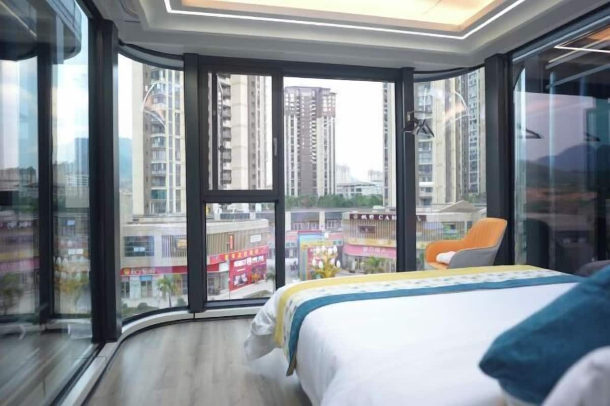 Una habitación de hotel con un muro de cristal curvo, una cama y una silla.