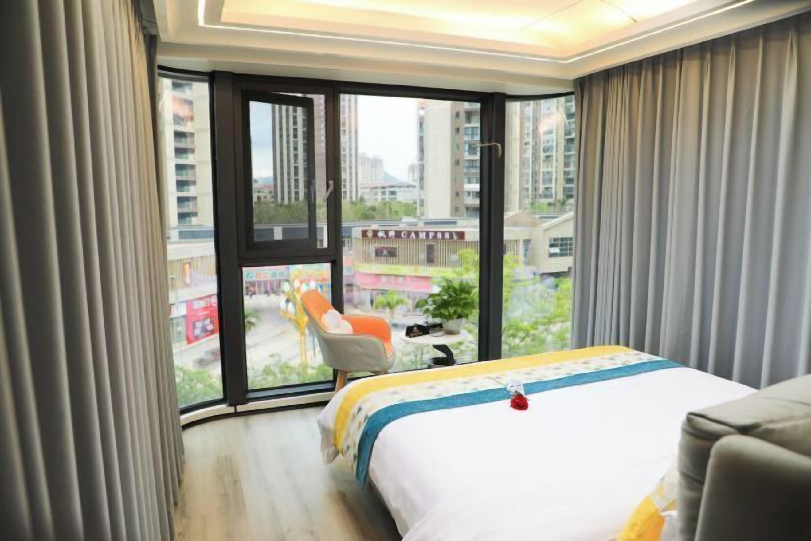 Ein Hotelzimmer mit Bett, Sessel und Blick auf die Stadt durch große Fenster.