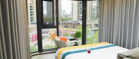 A hotel room with a bed, a chair, and a view of the city through large windows.