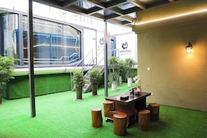 A room with a green carpet, wooden stools, a table, and a staircase leading to a balcony. - Luodian Anbang Garden Hotel (Luodian)
