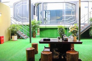 Une pièce dotée d’un sol recouvert d’un gazon synthétique vert, d’une table en bois avec des tabourets et de plantes en pot.
