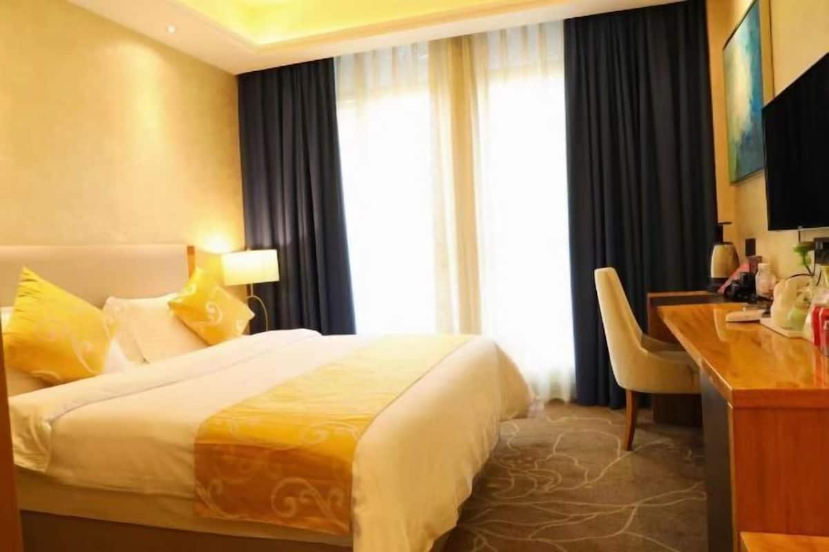 Habitación de hotel con cama, escritorio, silla, lámpara y televisor.