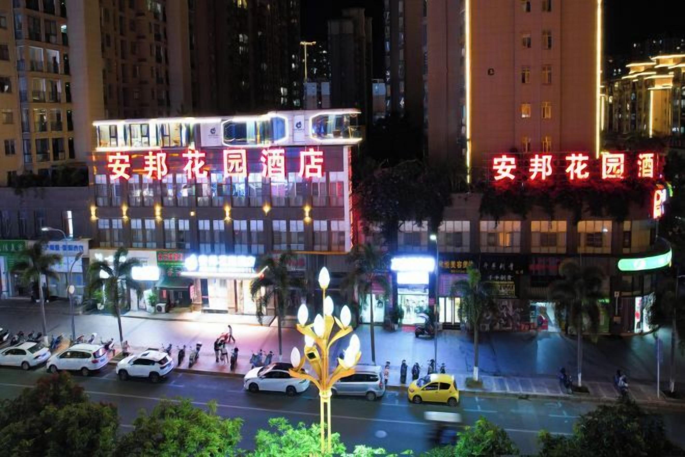 Un hotel con señalización iluminada, vista de la calle con coches estacionados y una farola decorativa.