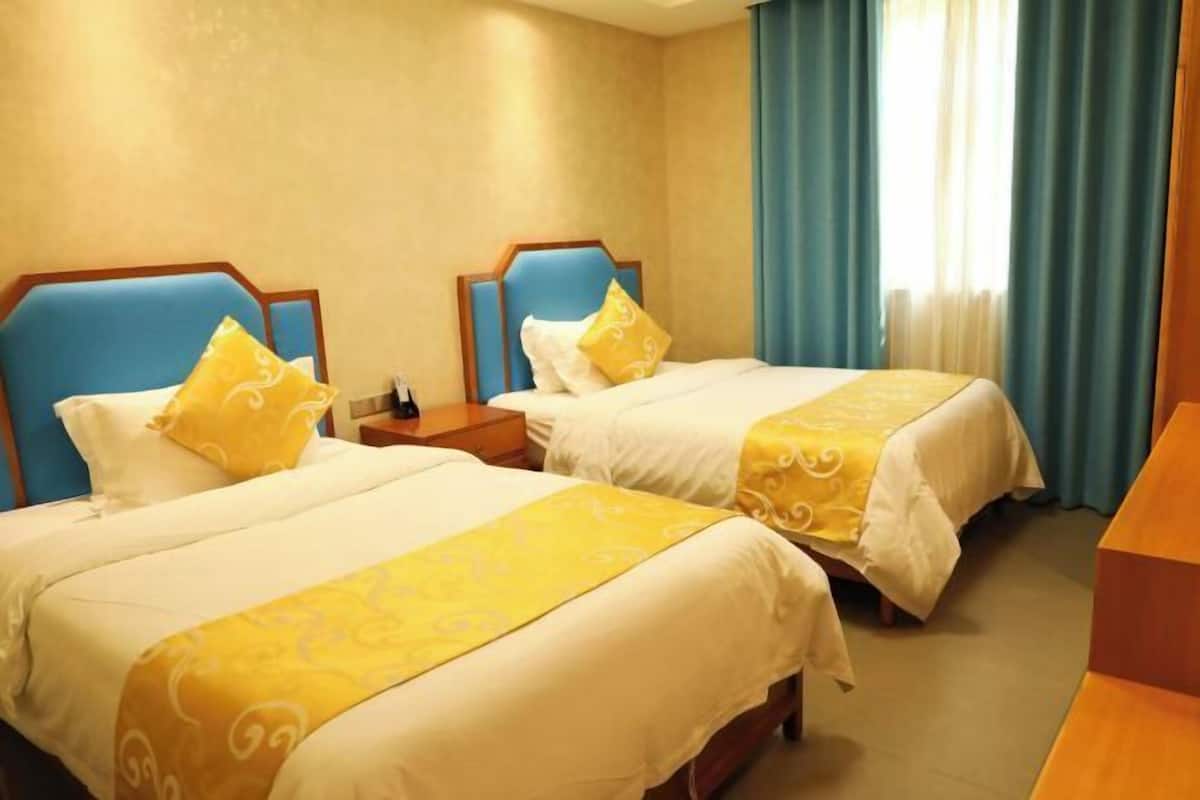 Habitación de hotel con dos camas, cada una con cabecera azul y ropa de cama blanca.