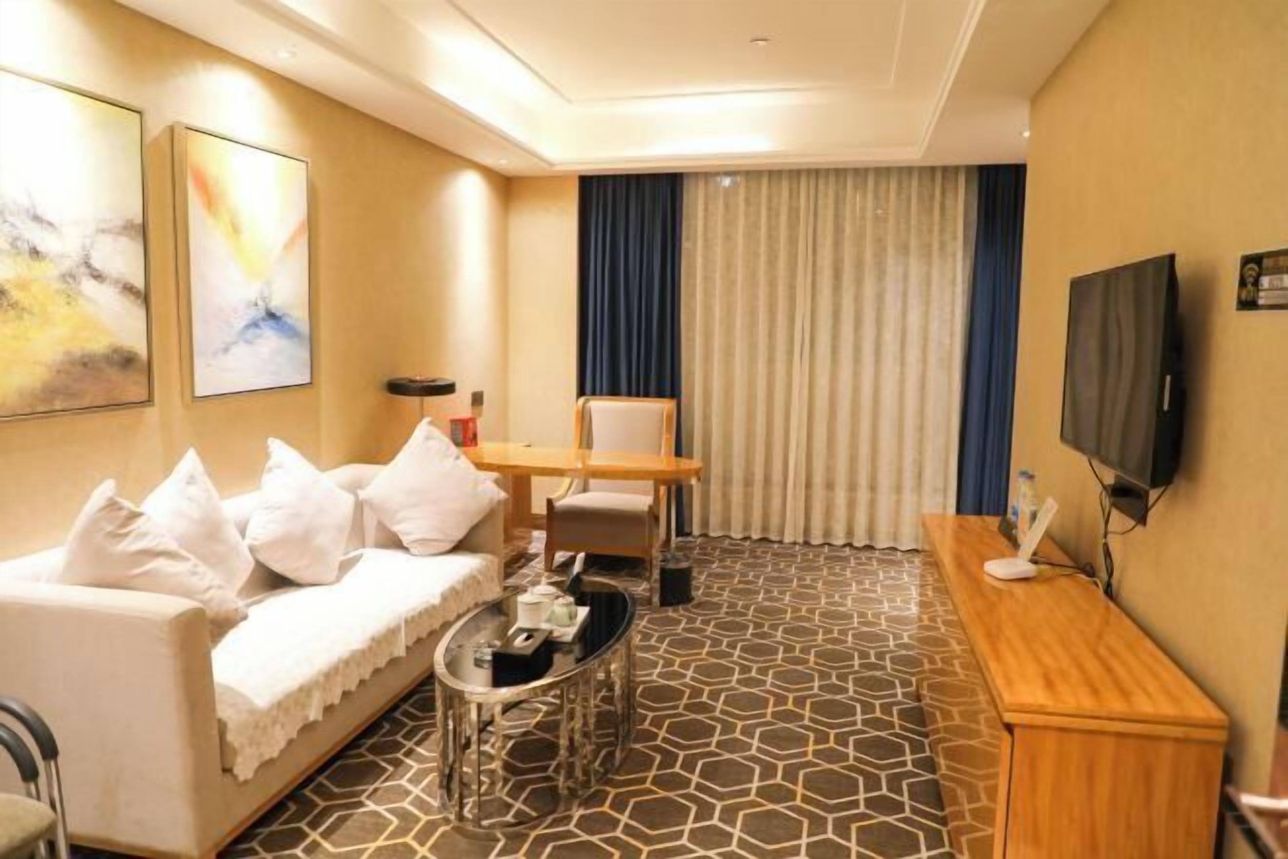 Habitación de hotel con sofá, una mesita, televisor y ventana con cortinas.