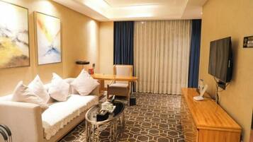 Habitación de hotel con sofá, una mesita, televisor y ventana con cortinas.