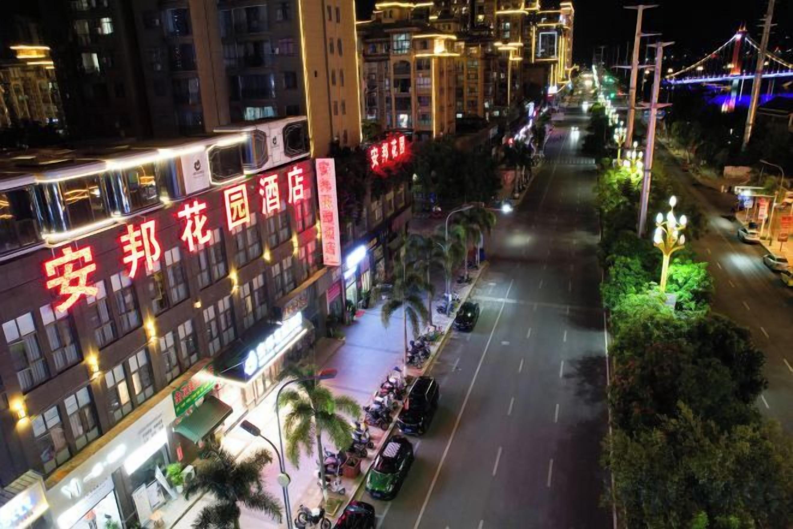 A multi-story building with illuminated signage, a street in front, and a bridge in the background.