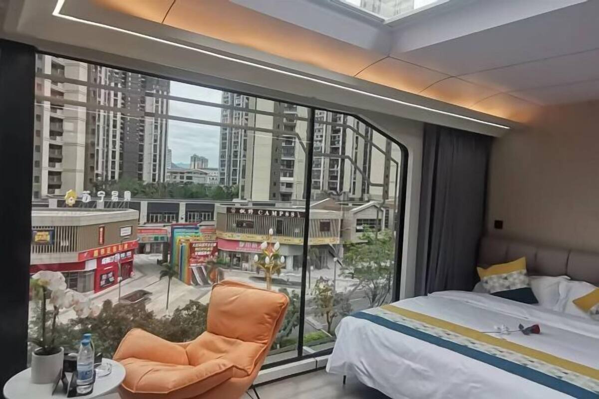 Habitación de hotel con una ventana grande, una cama, una silla y una mesita con una botella de agua.