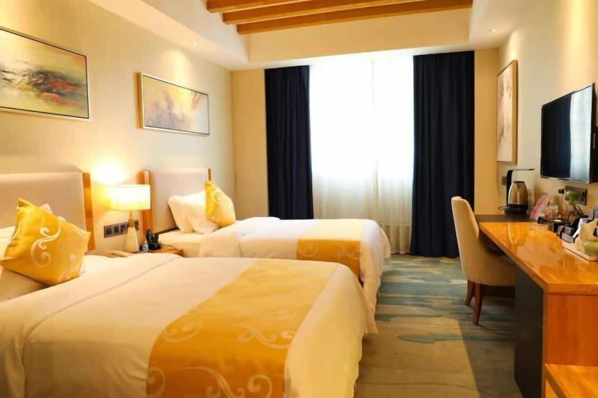 Una habitación de hotel con dos camas, un escritorio, una silla, un televisor y obras de arte en las paredes.