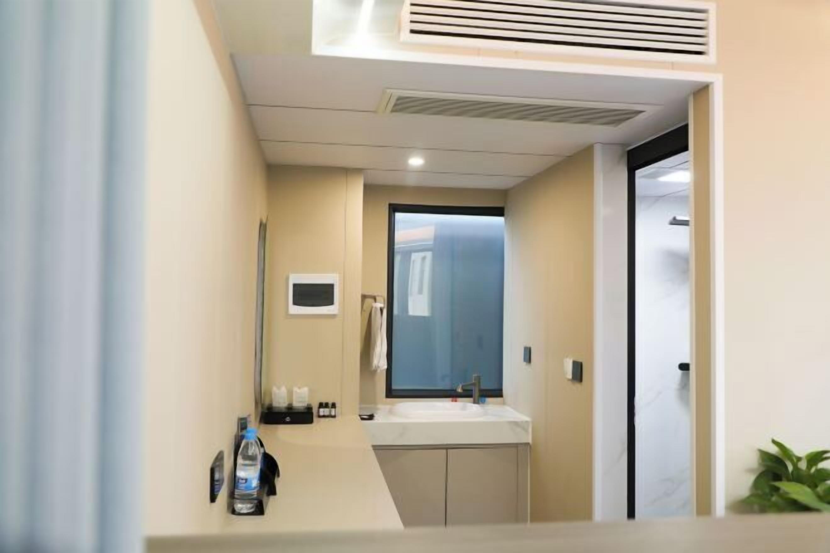 Un baño moderno con lavamanos, espejo y una ventana pequeña.
