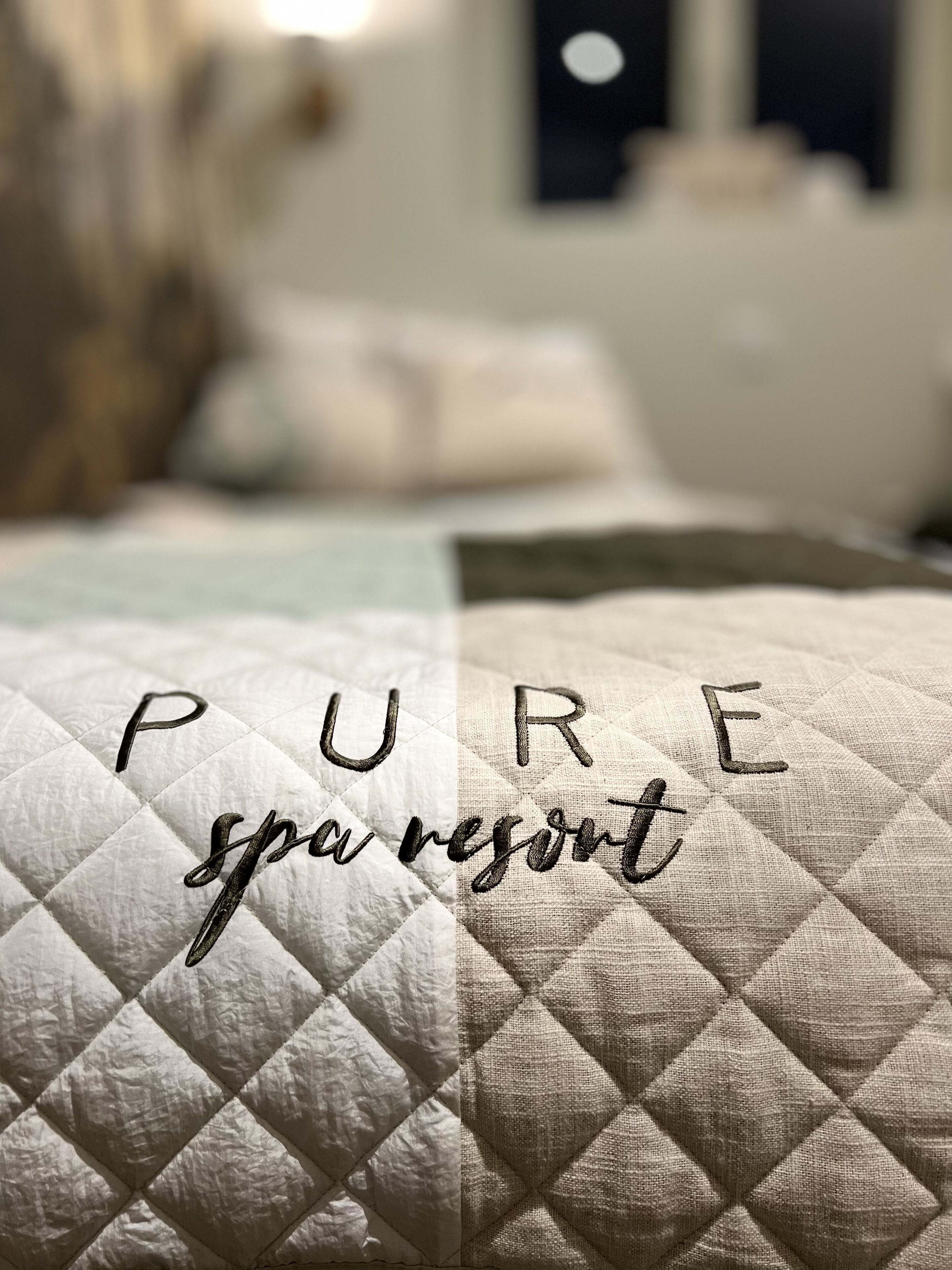 A bed with a quilted cover and embroidered text reading "PURE spa resort".