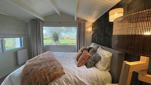 Un dormitorio con cama, cortinas, vistas al exterior y una lámpara de pared.